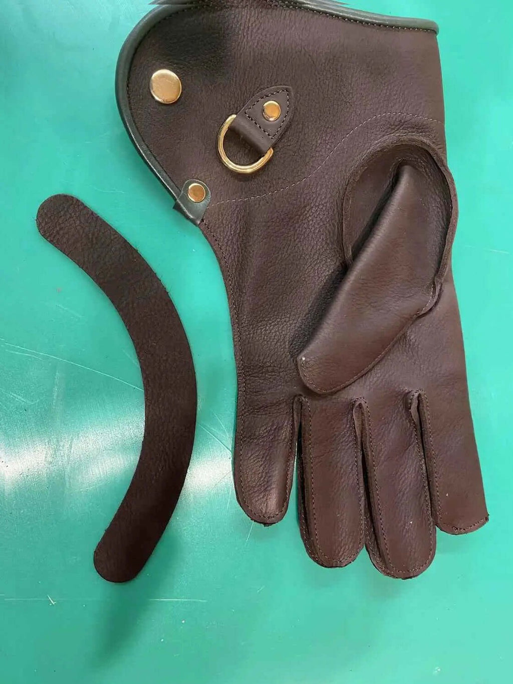 Machine sewn falconry gloves resting on a green surface with a brown leather cuff.