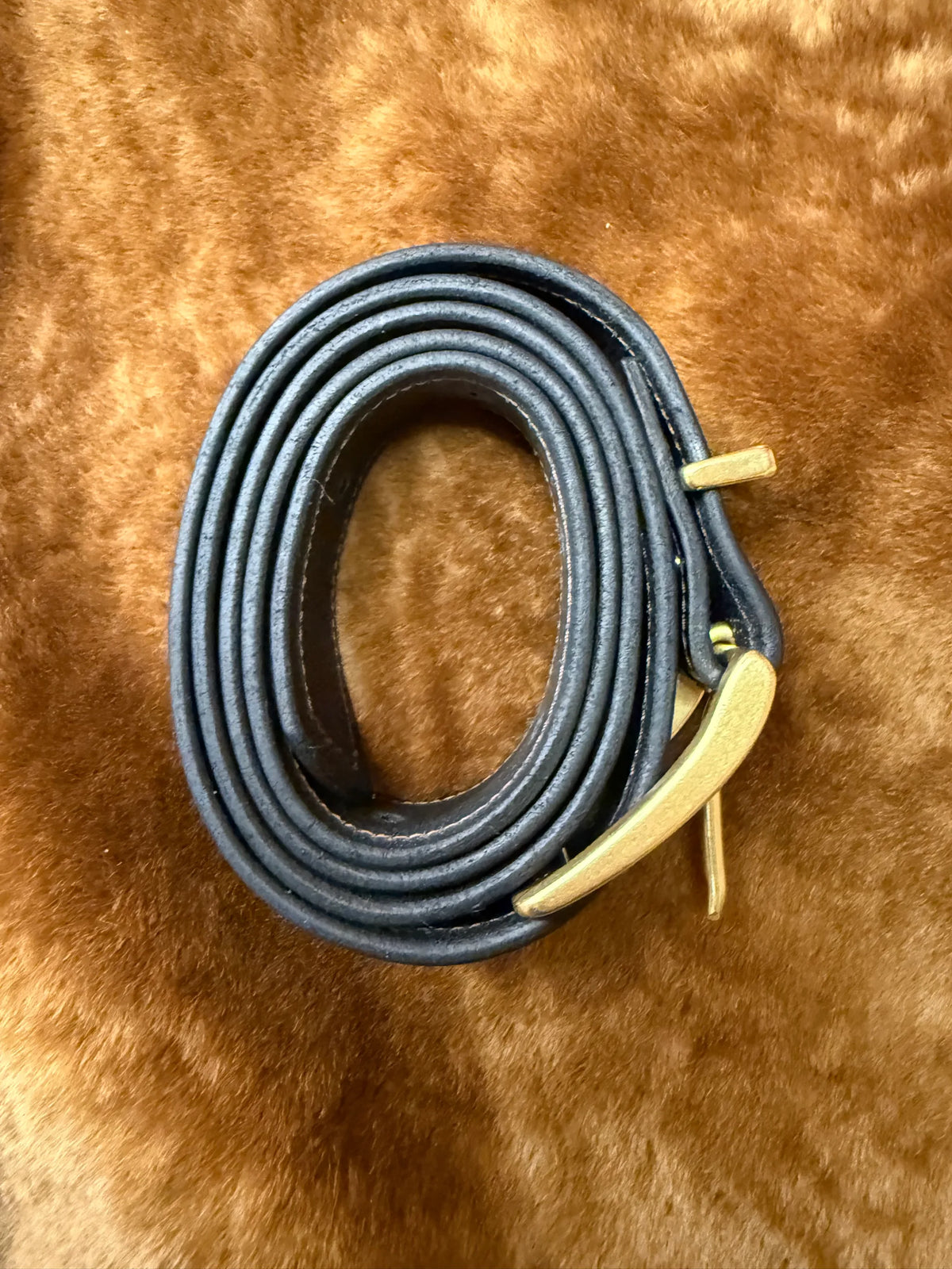 Premium leather belts for everyday use rolled up with a gold buckle on a soft background.