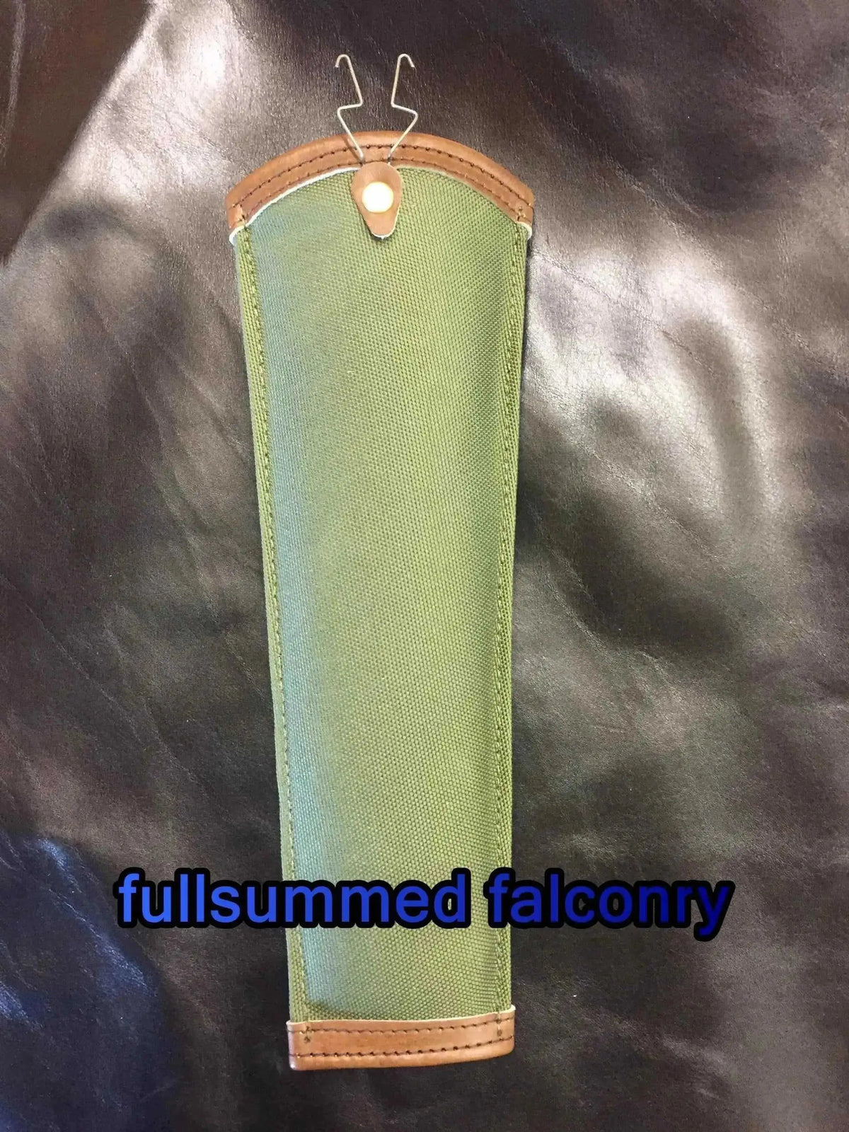 Olive green falconry tail guard with tan leather trim and metal wire clip attachment